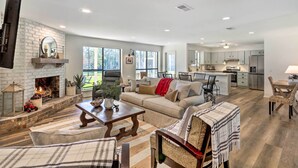 A spacious living room with a fireplace, a sofa, and a dining area with chairs. - 'green Acres' Home w/ Fire Pit + Fishing Pond (Molino)
