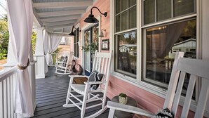 Une véranda avec des fauteuils à bascule blancs, une petite table et une plante en pot.