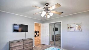 A bedroom with a bed, a ceiling fan, a TV, a dresser, and a door leading to a hallway.