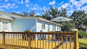 A wooden deck with a railing, a covered patio area, and a house in the background.