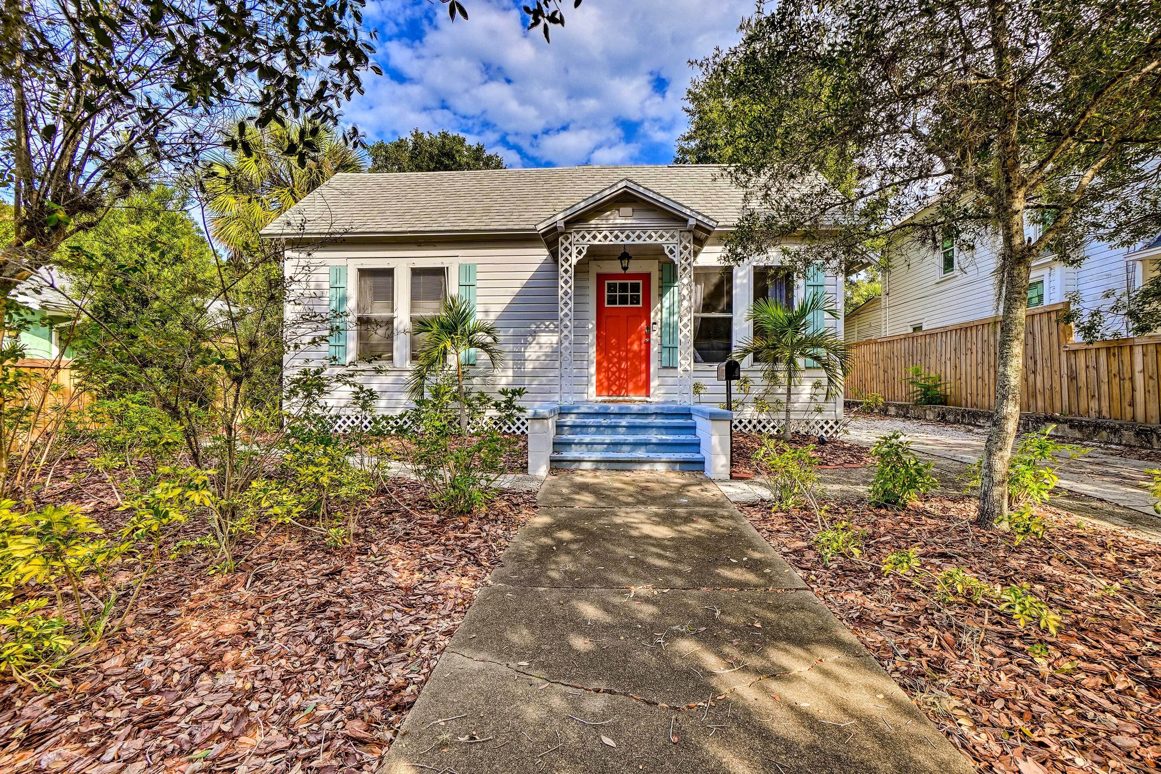 A house with a red door, a front porch, and a small front yard with trees and mulch.