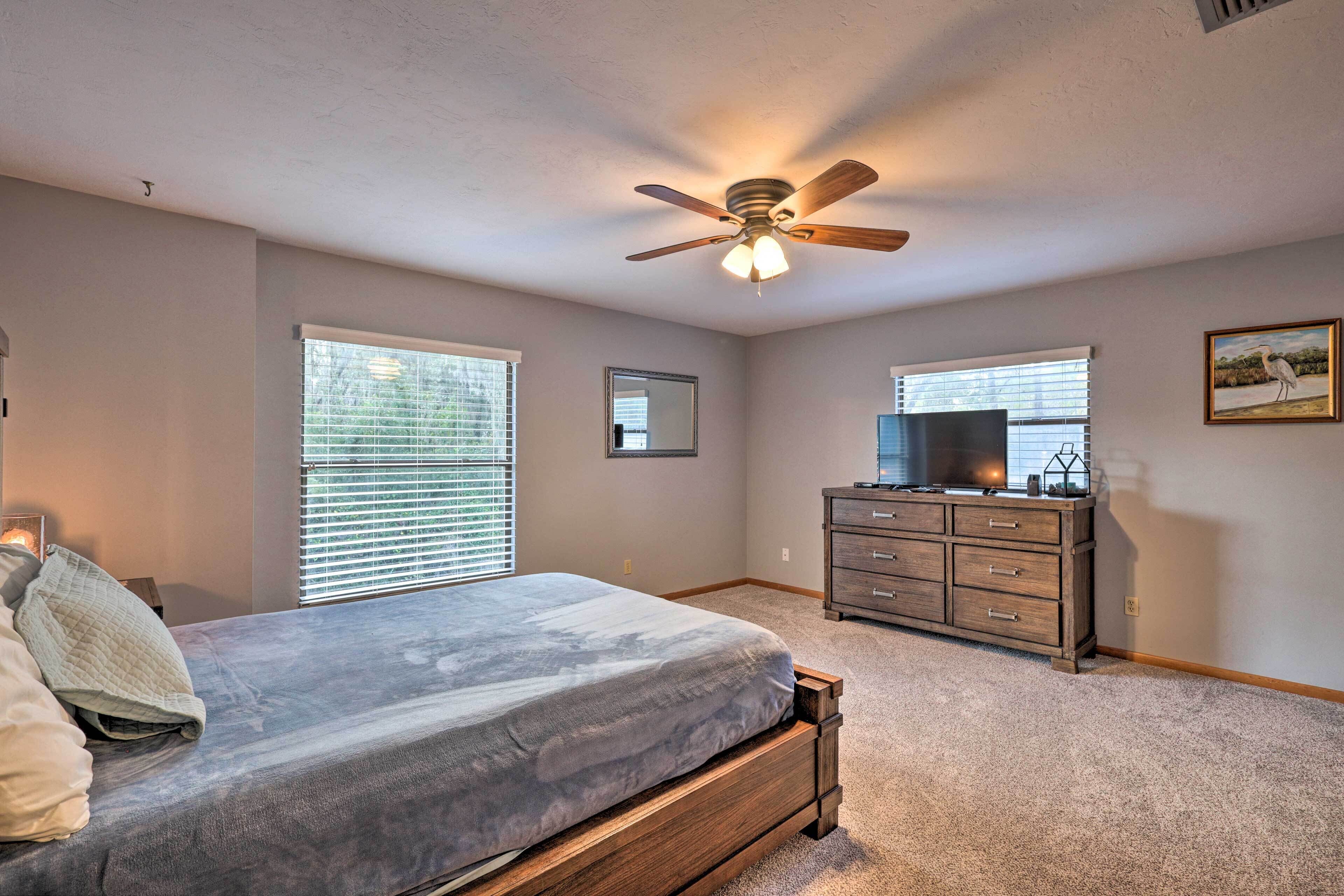 A bedroom with a bed, a dresser, a ceiling fan, and two windows with blinds.
