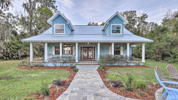 A two-story house with a blue roof and white trim, a front porch with a bench, and a brick pathway leading to the entrance. - 20 Mi to UF Campus: Santa Fe Lake Escape w/ Dock! (Earleton)