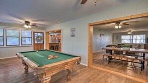 A pool table in a room with wooden floors and ceiling fans, a dining area with a table and chairs, and a door leading to another room. - 20 Mi to UF Campus: Santa Fe Lake Escape w/ Dock! (Earleton)