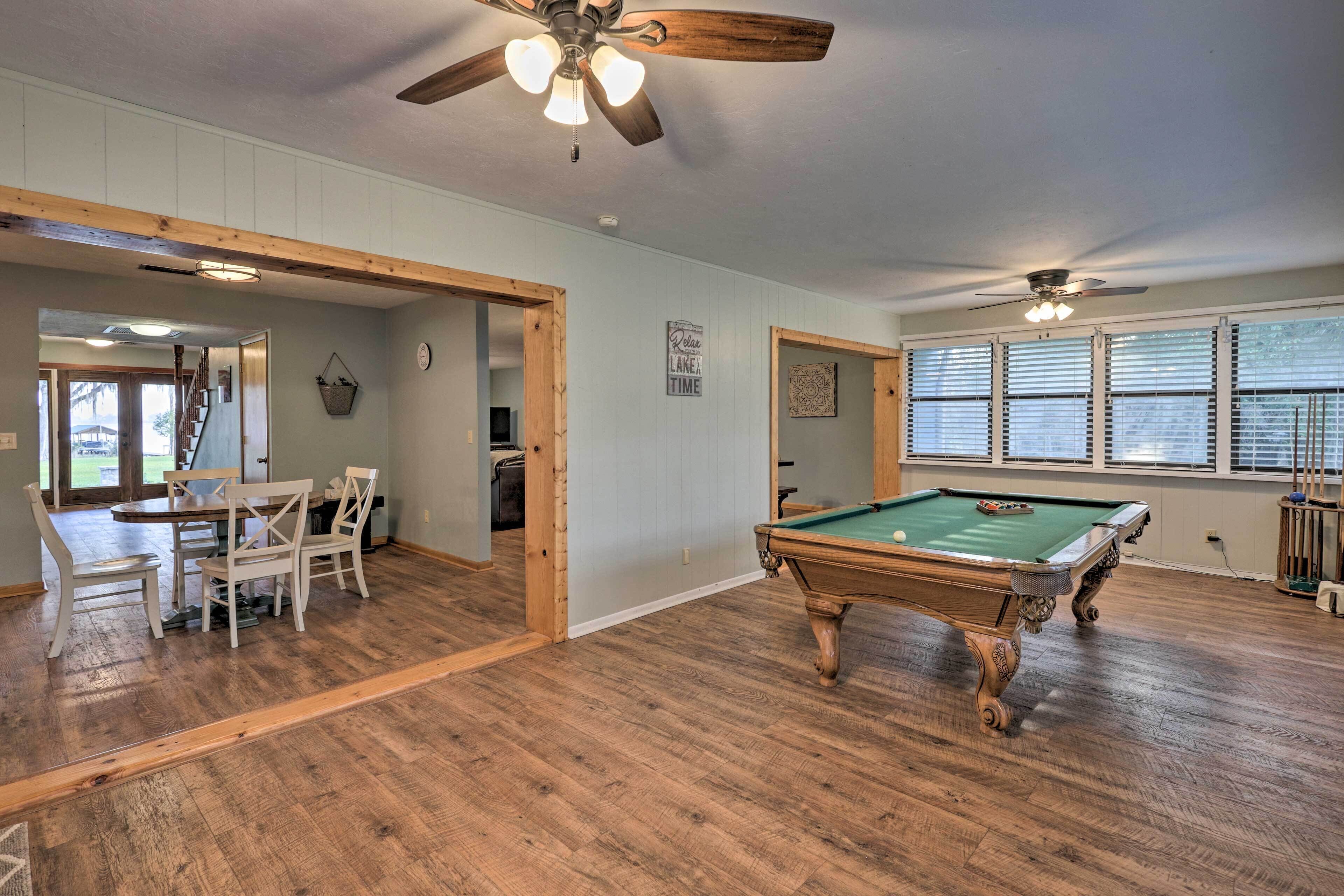 Une pièce spacieuse équipée d’une table de billard, d’un plancher en bois, de ventilateurs de plafond et d’un coin repas avec des chaises.