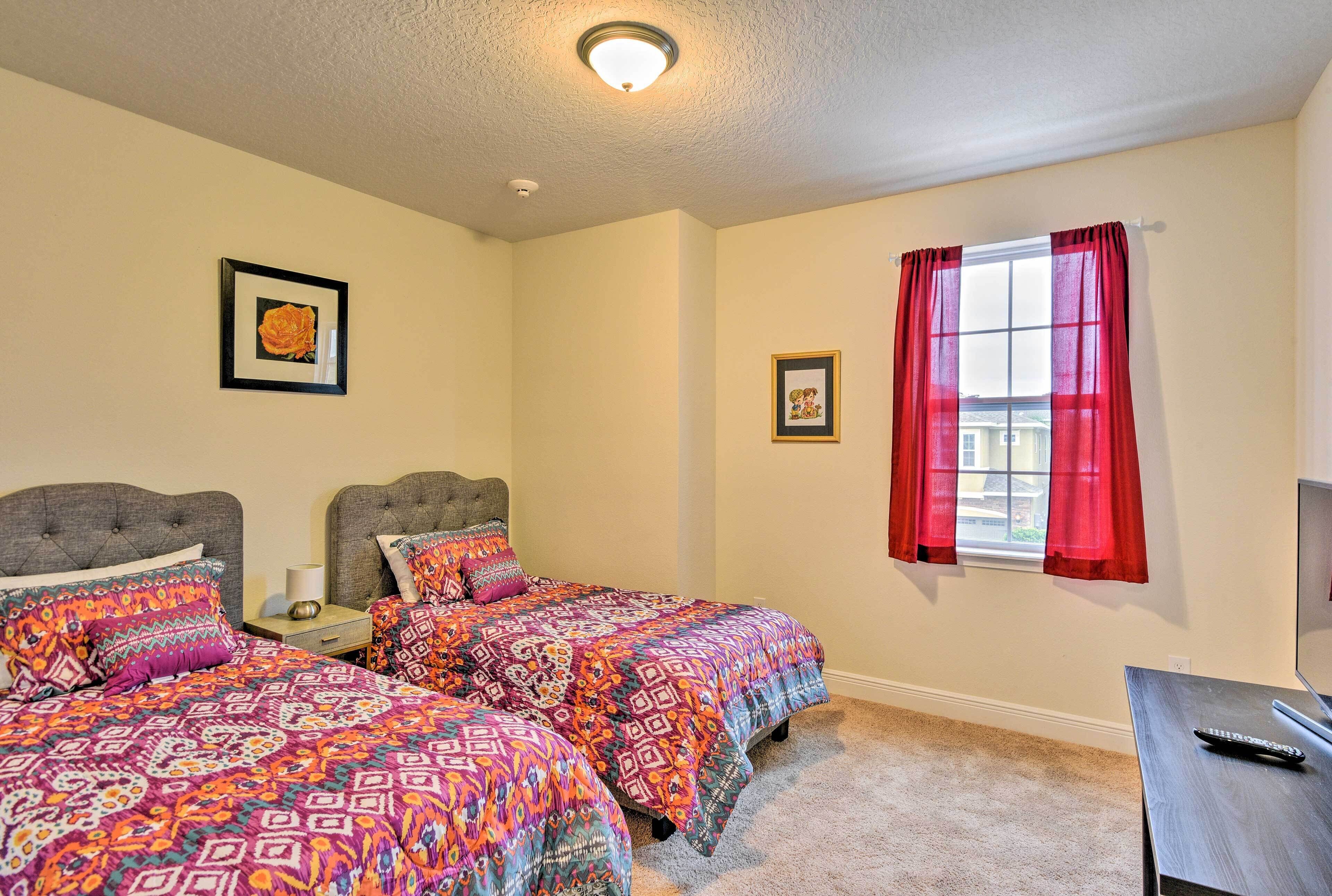 A bedroom with two beds, a window with red curtains, a ceiling light, and a TV on a stand.