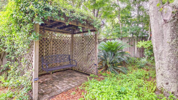 A wooden pergola with a bench, surrounded by lush greenery and a wooden fence. - 5 Mi to Pensacola Beach: Townhome w/ Yard! (Gulf Breeze)