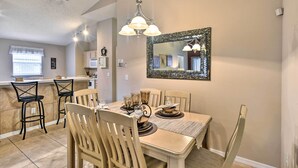 A dining area with a table set for four, surrounded by wooden chairs. A chandelier hangs above the table, and a large mirror is mounted on the wall. - Clermont Home w/ Pool & Game Room: 10 Mi to Parks! (Clermont)