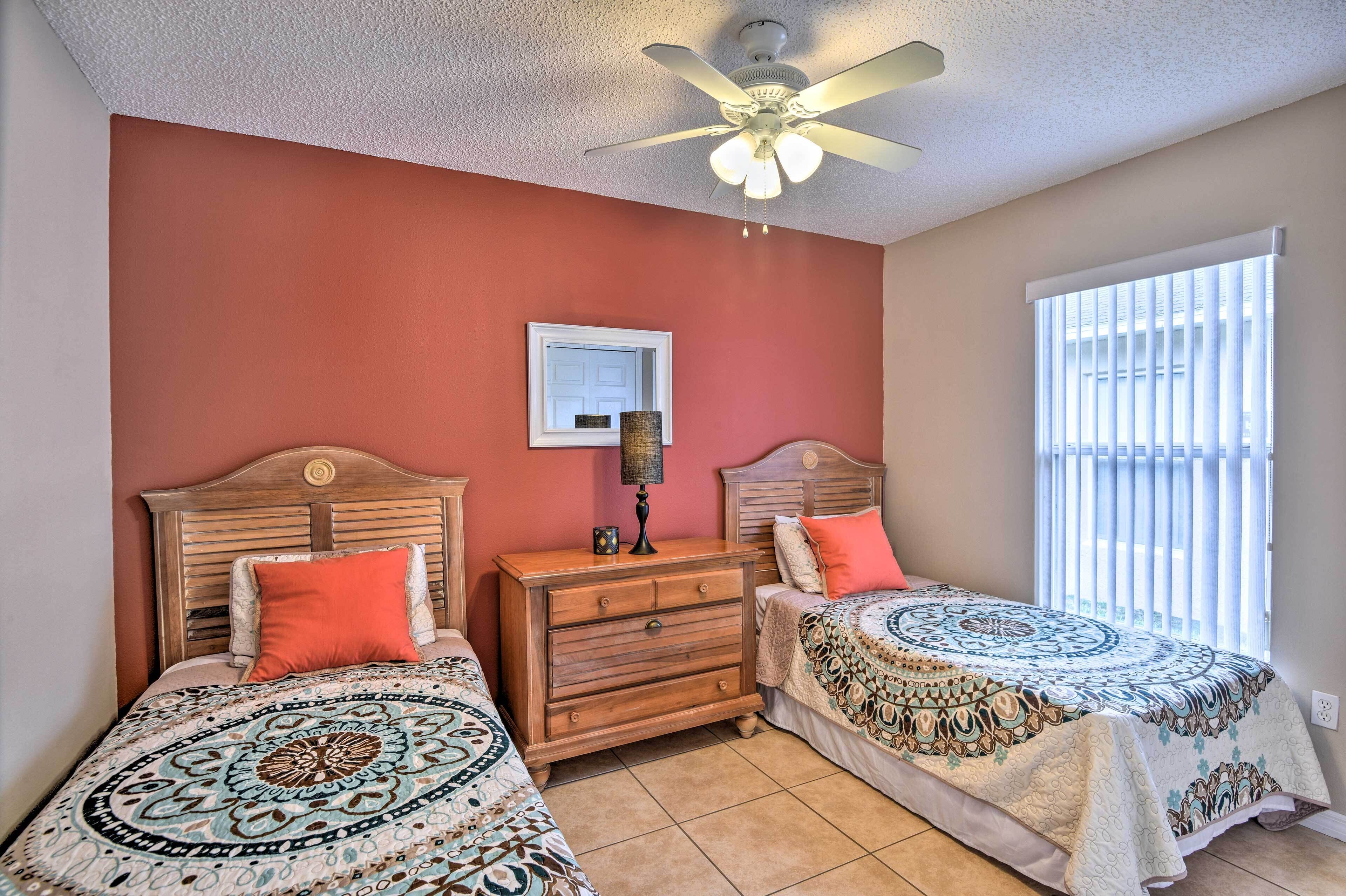 A bedroom with two beds, a ceiling fan, a dresser, and a window with blinds.