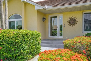 A house with a yellow facade, a front door with glass panels, a small porch, and a decorative sun on the wall. - Walk to Beach & JW! Marco Island Pool Haven (Marco Island)