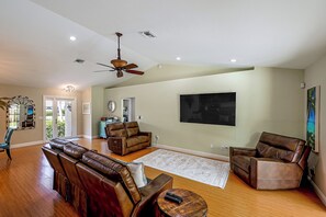 A spacious living room with a ceiling fan, a large flat-screen TV, and leather sofas.