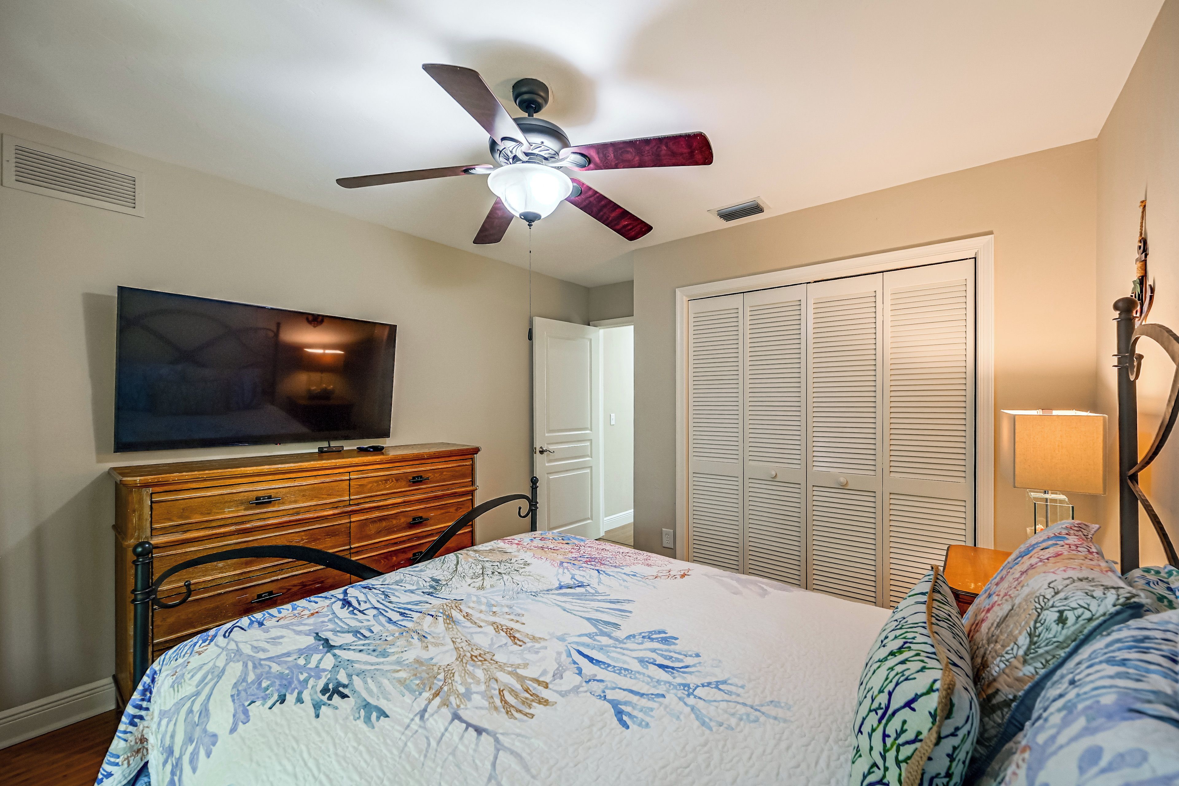 Une chambre à coucher avec un lit, un téléviseur posé sur une commode, un ventilateur de plafond et une armoire.