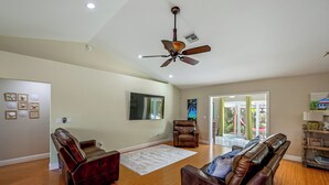 A spacious living room with a ceiling fan, a large flat-screen TV, and a view to the outside.