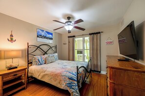 A bedroom with a bed, a ceiling fan, a television, and a window with curtains.
