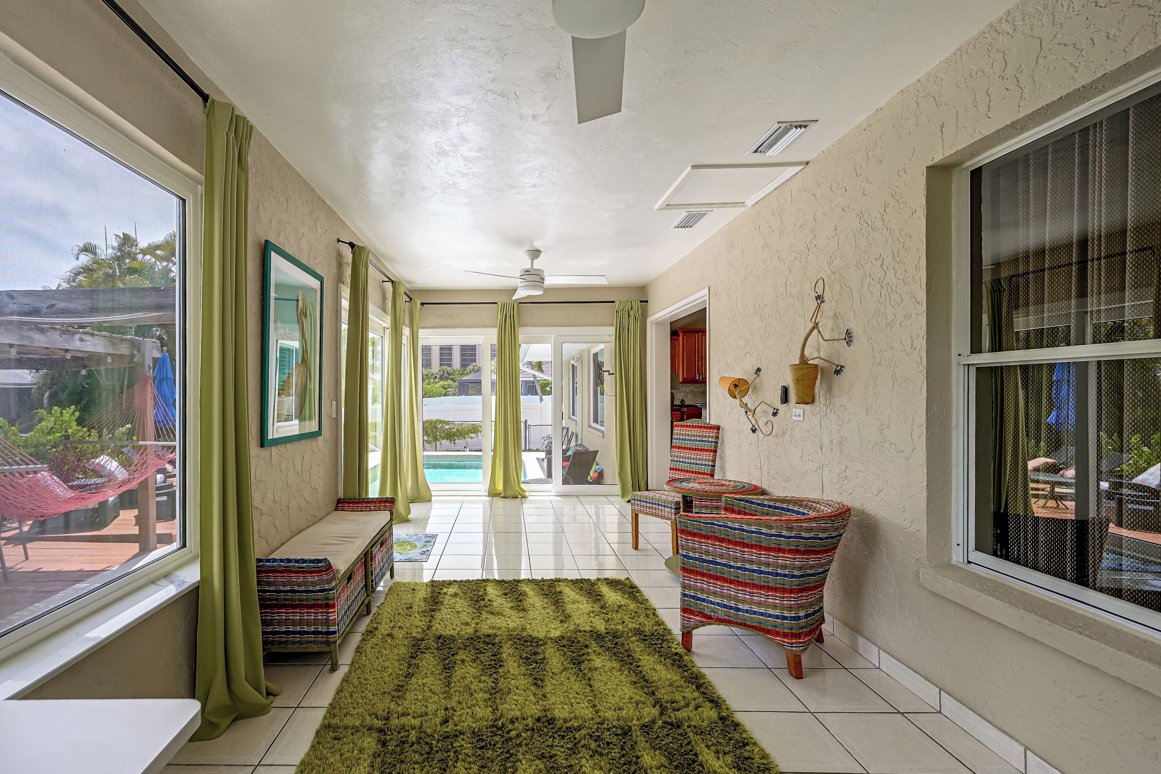 A hallway with a view of a swimming pool, a hammock, and a striped chair.