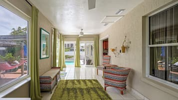 A hallway with a view of a swimming pool, a hammock, and a striped chair.