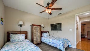A bedroom with two beds, a ceiling fan, a TV, and a wooden wardrobe.