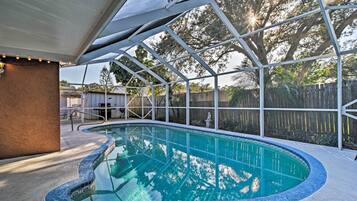 A swimming pool with a curved edge, surrounded by a covered area with a metal frame and string lights.