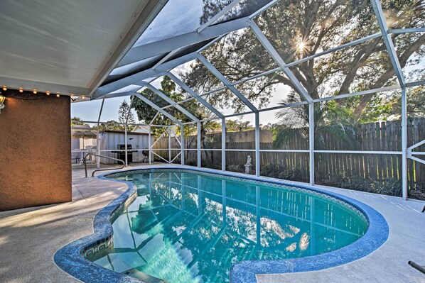 Una piscina con borde curvo, rodeada por una zona techada con estructura metálica y luces colgantes.