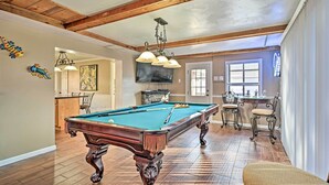 Een ruime kamer met een pooltafel, houten vloer en een eethoek met stoelen en een tafel.