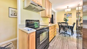 A kitchen with wooden cabinets, a black stove, and a dining area with a table and chairs. - Jacksonville Getaway w/ Yard ~ 2 Mi to Beach! (Atlantic Beach)
