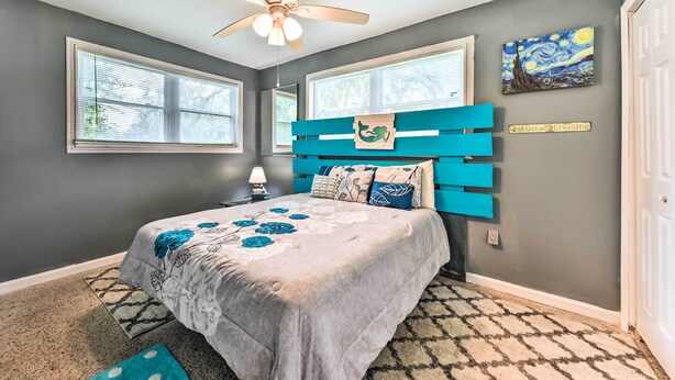 A bedroom with a bed, a ceiling fan, two windows, a painting, and a sign. - Jacksonville Getaway w/ Yard ~ 2 Mi to Beach! (Atlantic Beach)