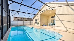 A swimming pool with a glass enclosure, a covered patio area, and a building with a beige exterior. - Kissimmee Escape w/ Lanai & Private Pool! (Kissimmee)