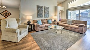 A spacious living room with a beige armchair, two brown sofas, a glass coffee table, and a large window providing natural light. - Kissimmee Escape w/ Lanai & Private Pool! (Kissimmee)