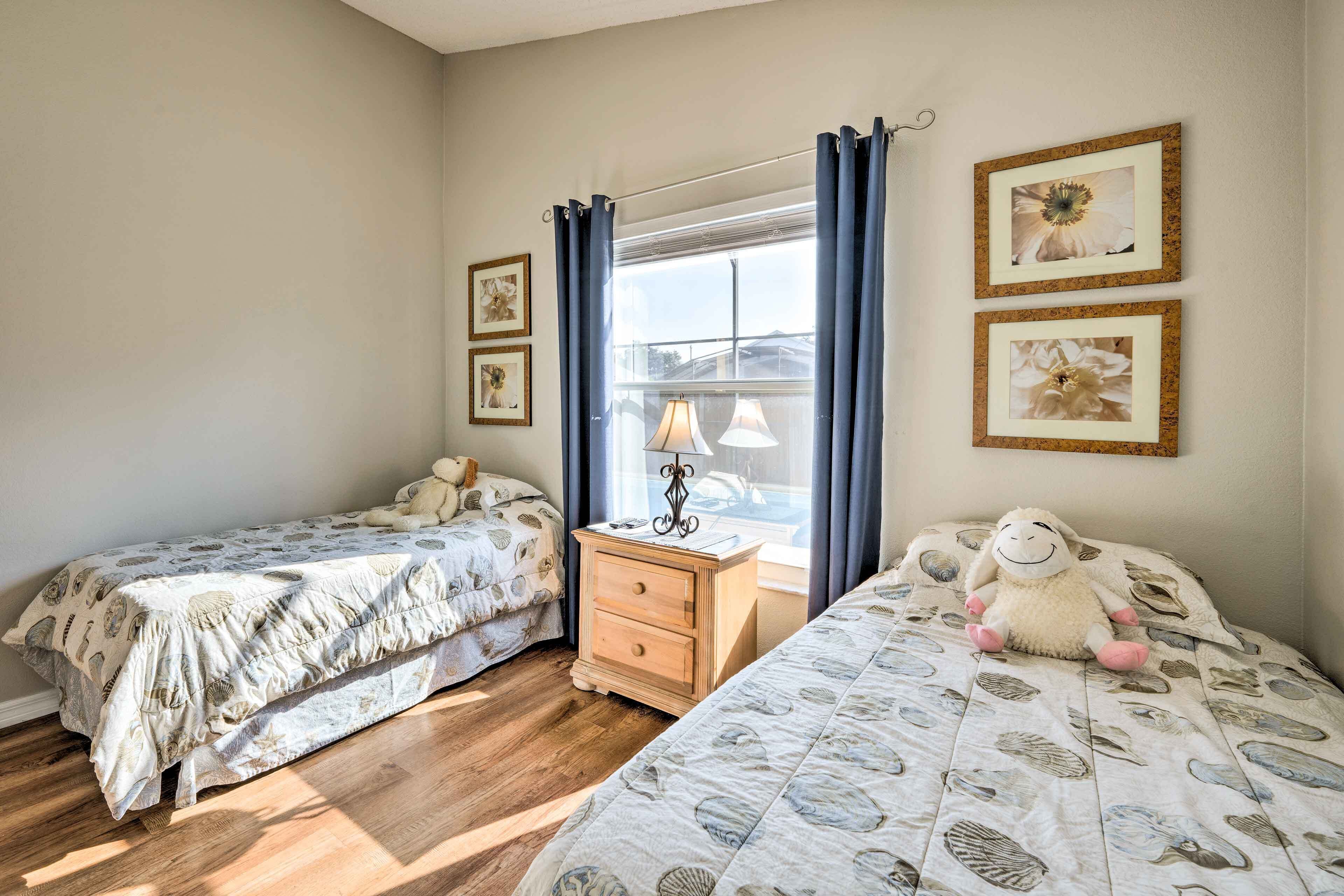 A bedroom with two beds, a nightstand, a lamp, and framed pictures on the wall.
