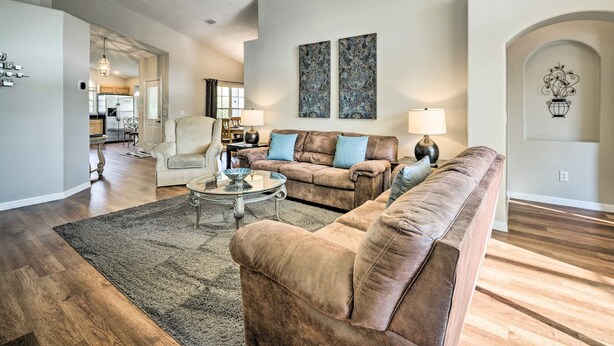 A spacious living room with a brown leather sofa, a glass coffee table, and a large rug. There are two wall-mounted lamps and a decorative wall piece. - Kissimmee Escape w/ Lanai & Private Pool! (Kissimmee)