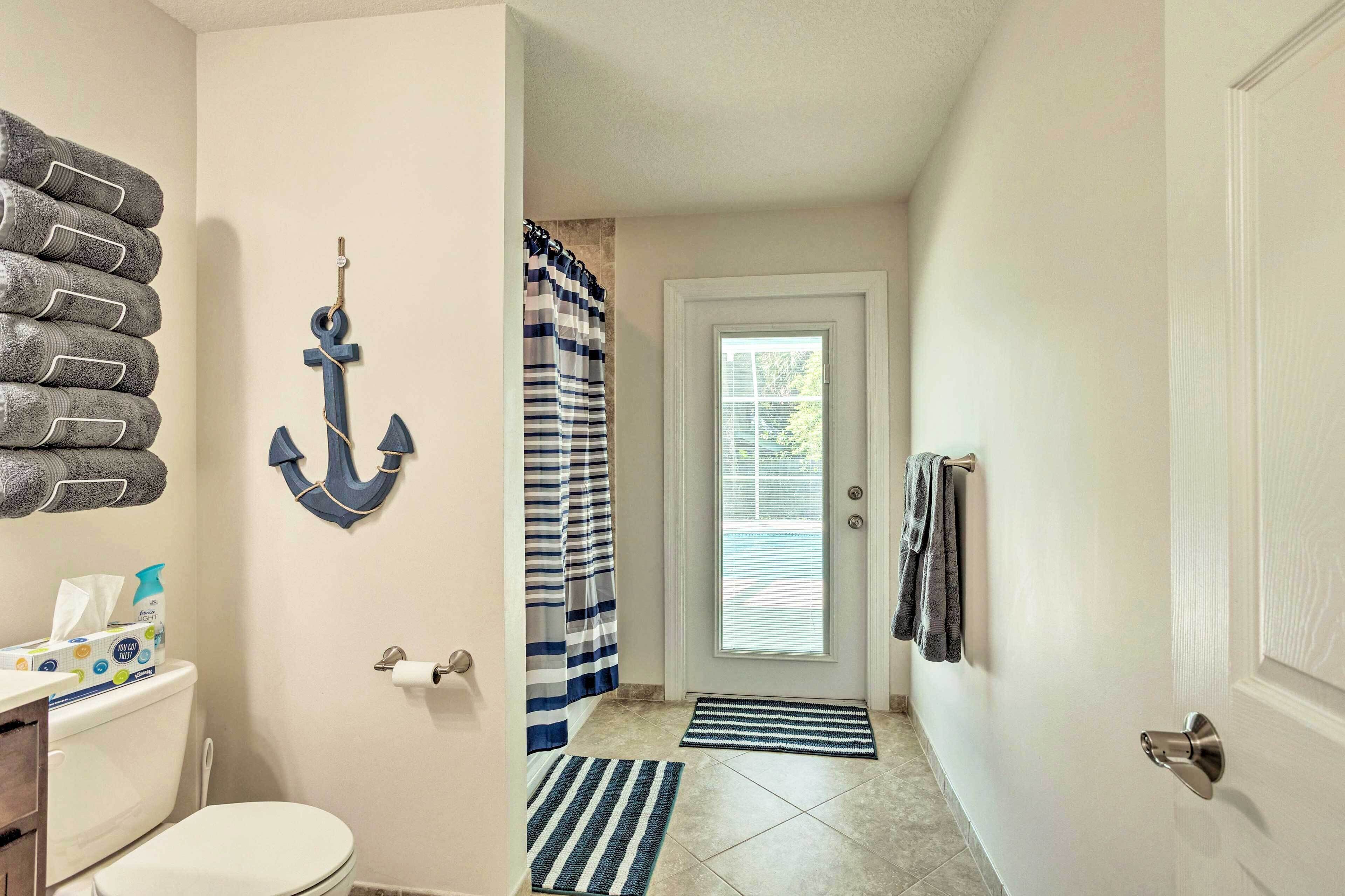A bathroom with a toilet, a towel rack, a striped shower curtain, and a door with a towel hanging on it.