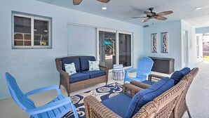 A covered outdoor seating area with wicker furniture and blue chairs, ceiling fans, and a view through glass doors. - Private Pool & Steps to Ocean: Island Beach House! (Fort Pierce)