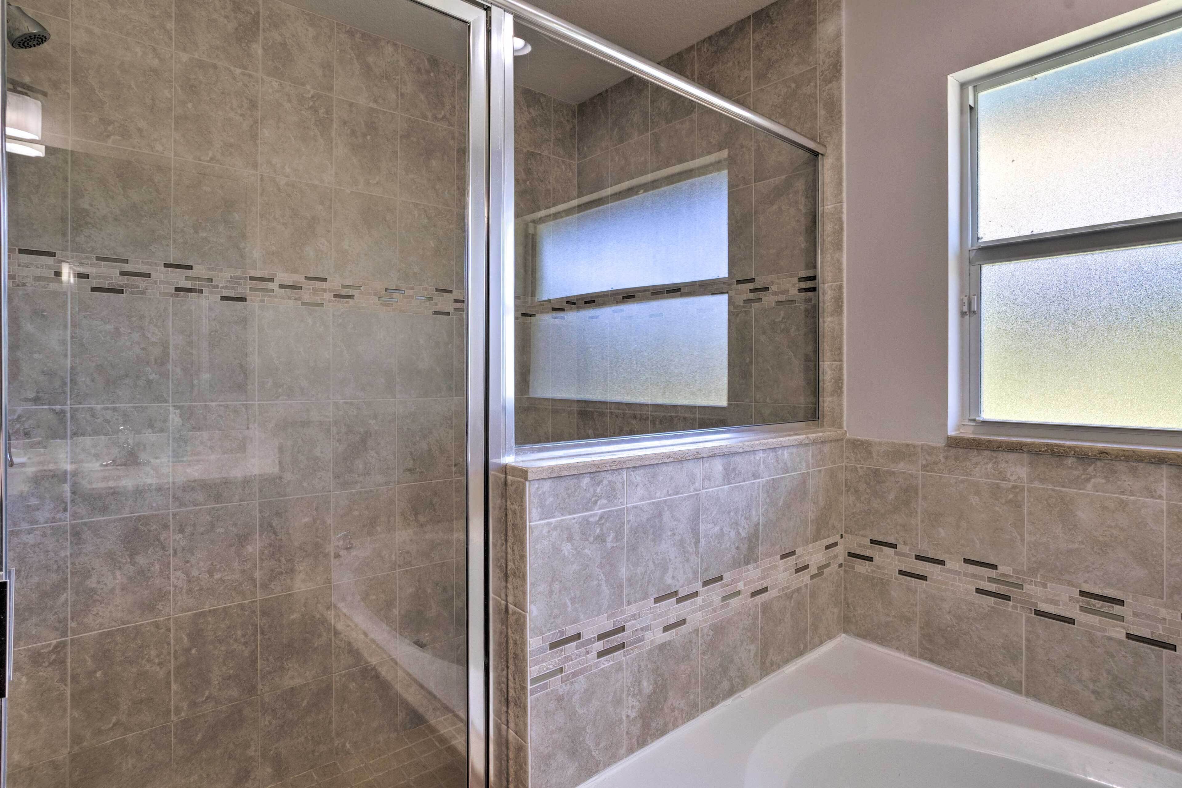 A bathroom with a glass shower enclosure, a bathtub, and a window.