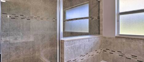 A bathroom with a glass shower enclosure, a bathtub, and a window.
