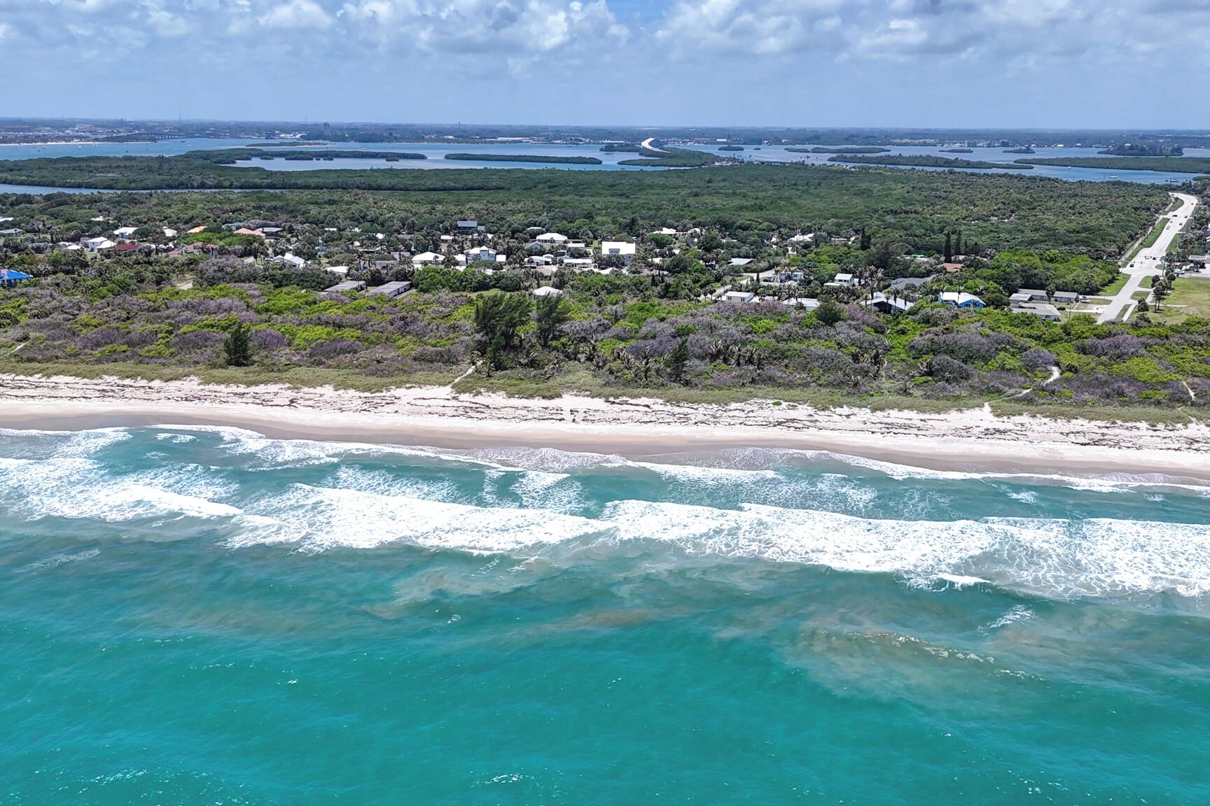Zona costera con playa, carretera y área residencial con casas.