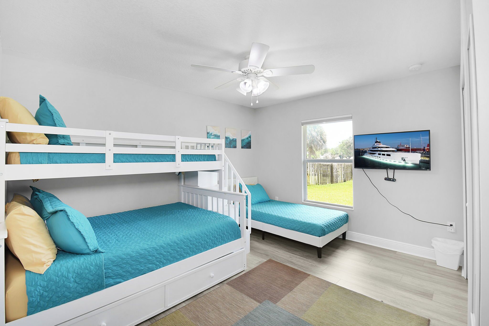 A room with bunk beds, a ceiling fan, a television, and a window with a view of a boat.