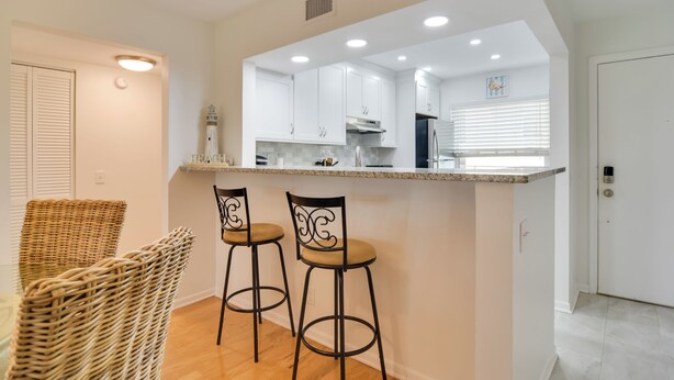 A modern kitchen with white cabinets, a granite countertop, and two bar stools. - ~ 2 Mi to St Pete Beach! Isla Del Sol Condo (St. Petersburg)