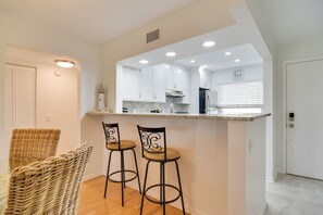 A modern kitchen with white cabinets, a granite countertop, and two bar stools. - ~ 2 Mi to St Pete Beach! Isla Del Sol Condo (St. Petersburg)