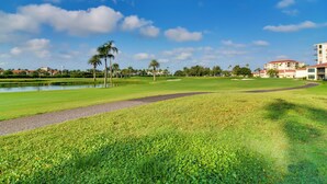 A golf course with a pond, palm trees, and a building in the background. - ~ 2 Mi to St Pete Beach! Isla Del Sol Condo (St. Petersburg)