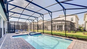 Une piscine entourée d’une structure en verre, bordée d’une terrasse en briques et d’une pelouse verdoyante.