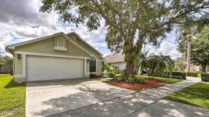 A single-story house with a garage, surrounded by a well-maintained lawn and mature trees. - Lakefront Brandon Home w/ Patio & Screened Lanai! (Brandon)