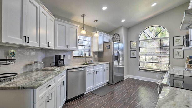 A modern kitchen with white cabinets, a stainless steel refrigerator, and a large window with blinds. - Lakefront Brandon Home w/ Patio & Screened Lanai! (Brandon)