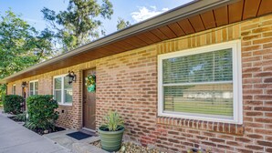 A brick house with a front porch, potted plants, and a small garden area.