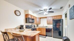 A kitchen with wooden cabinets, a black refrigerator, a microwave, and a ceiling fan.