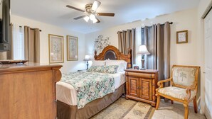A bedroom with a bed, a wooden chair, a nightstand, a ceiling fan, and a wall-mounted TV.