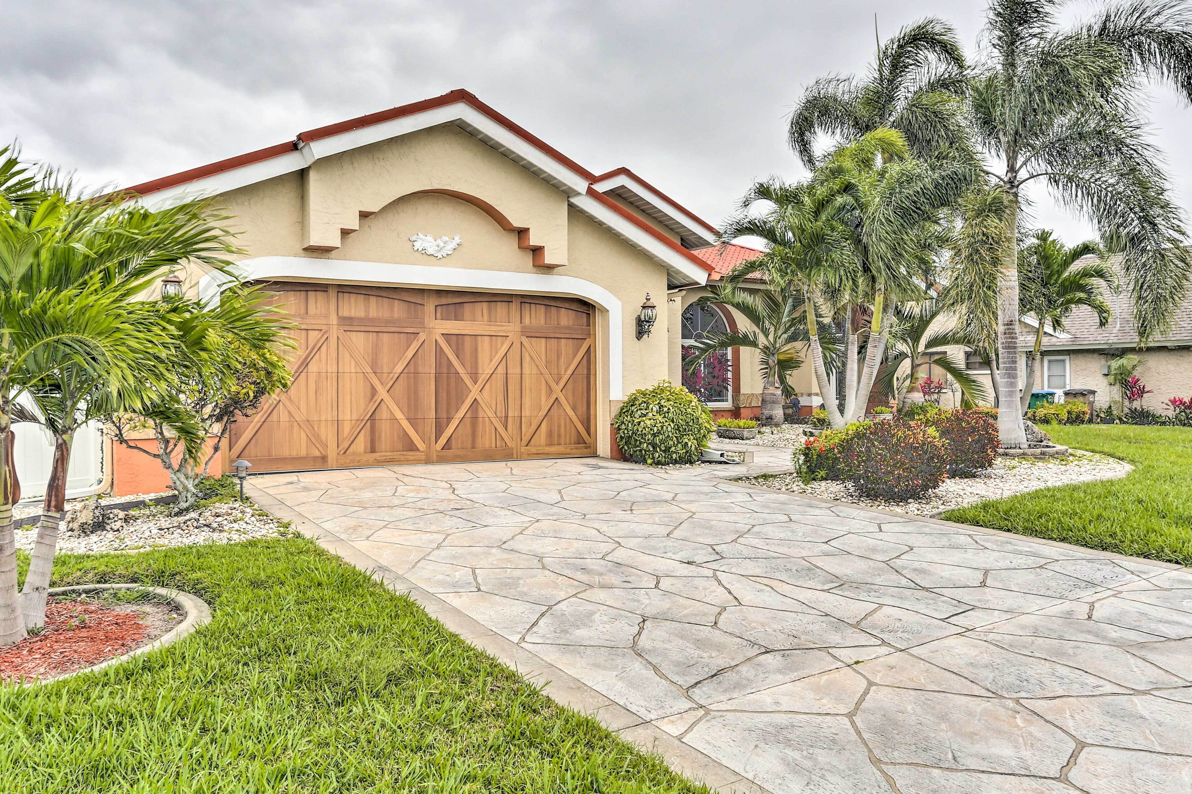 A house with a large wooden garage door, a stone driveway, and a well-maintained lawn with palm trees.