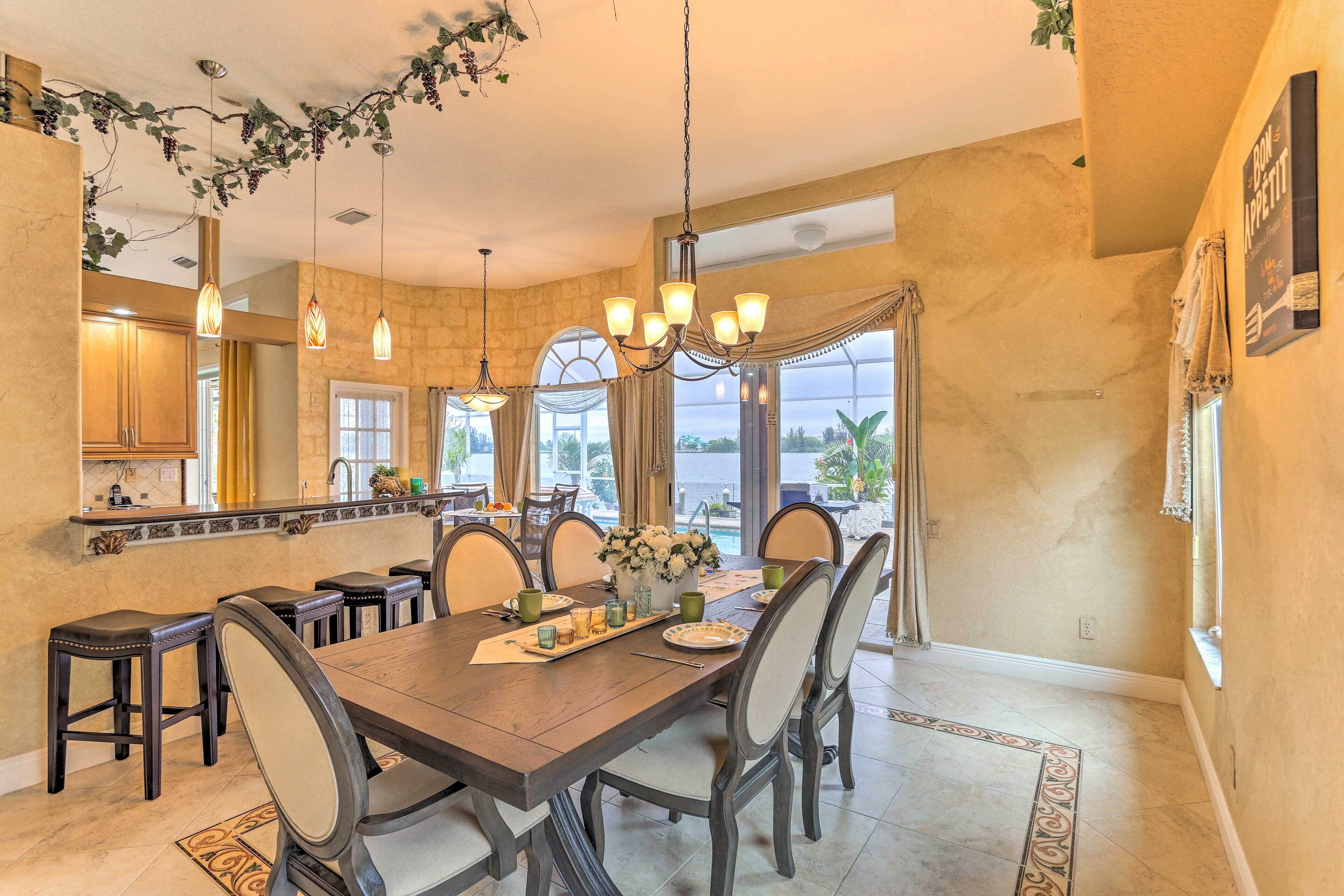 A dining area with a large wooden table, chairs, hanging lights, and a view of the outdoors.