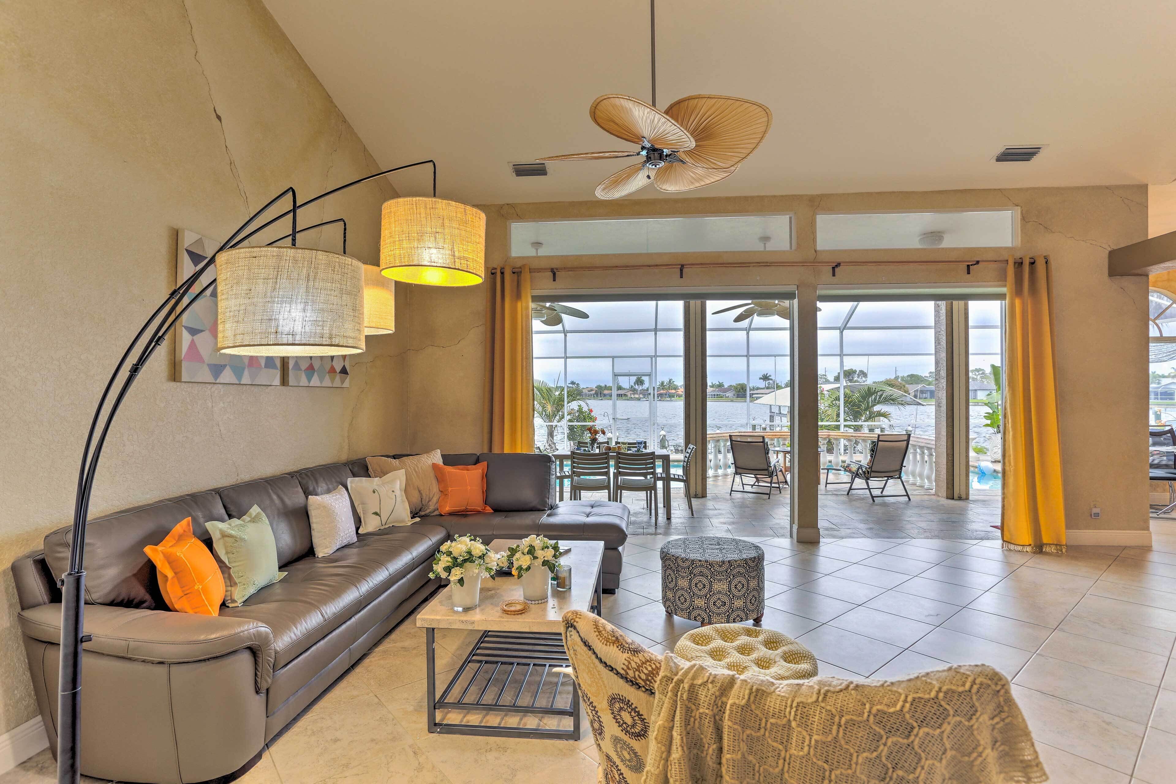 A spacious living area with a sofa, coffee table, and patterned ottoman. A ceiling fan and pendant lights are visible.