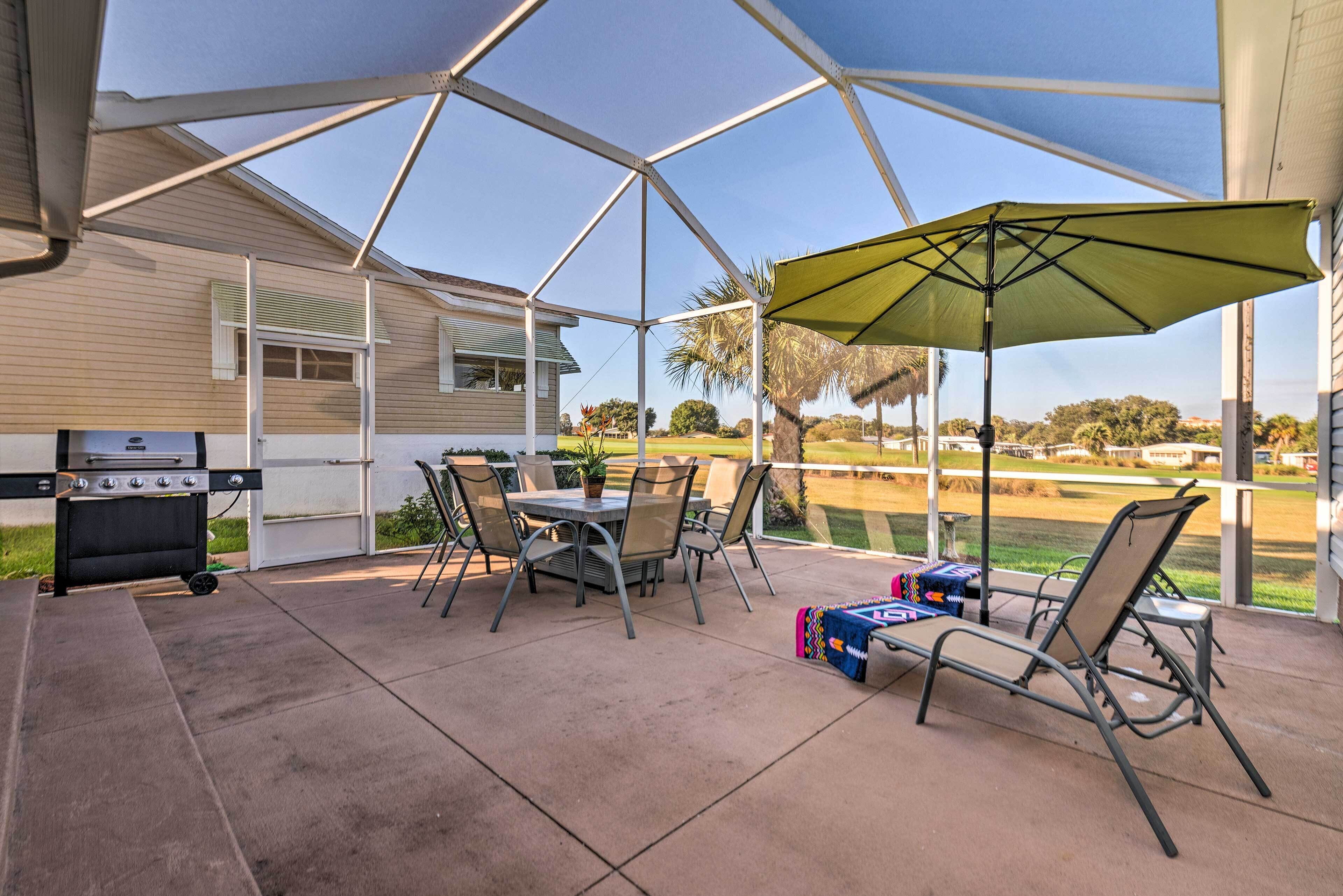 A covered patio with a grill, chairs, and an umbrella.