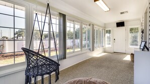 A spacious room with large windows, a hanging chair, a white door, and a white cabinet.
